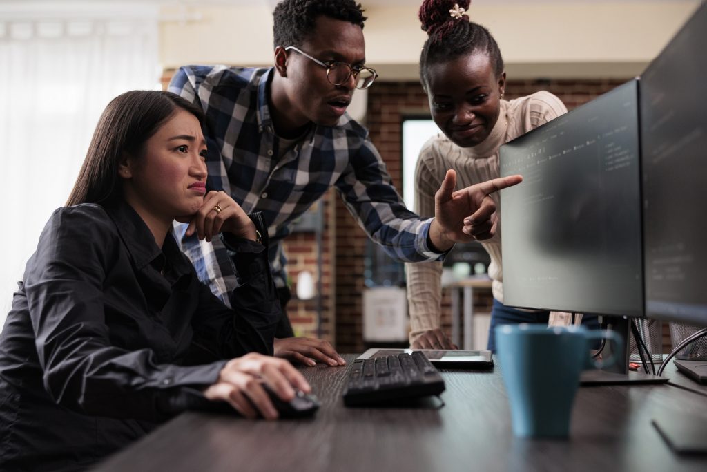 Team of 3 people looking at two monitors, pointing