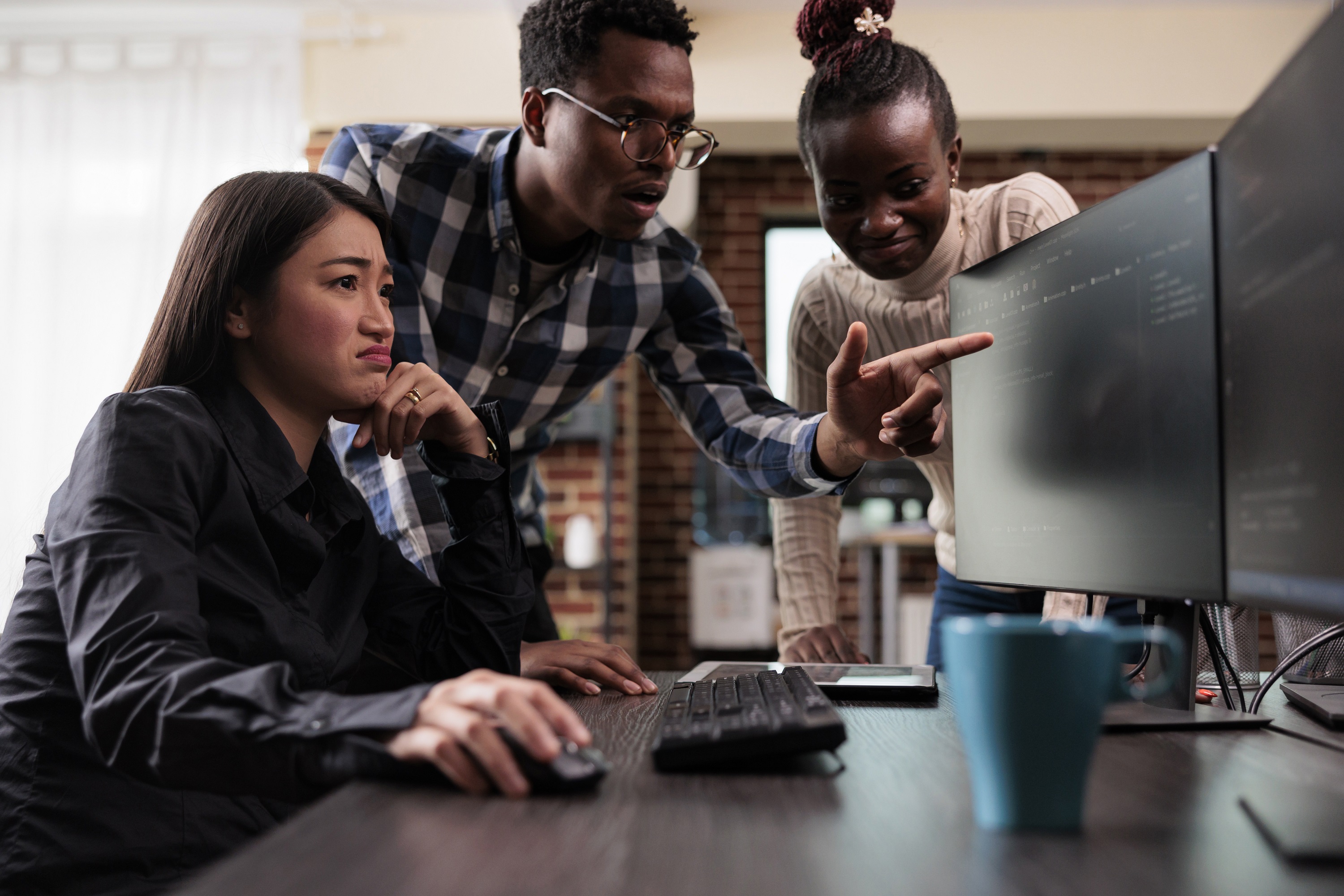 Team of 3 people looking at two monitors, pointing