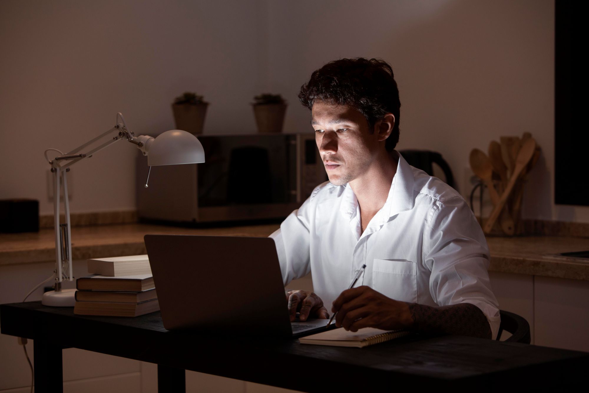 Man working late night in a dark office using laptop and notebook