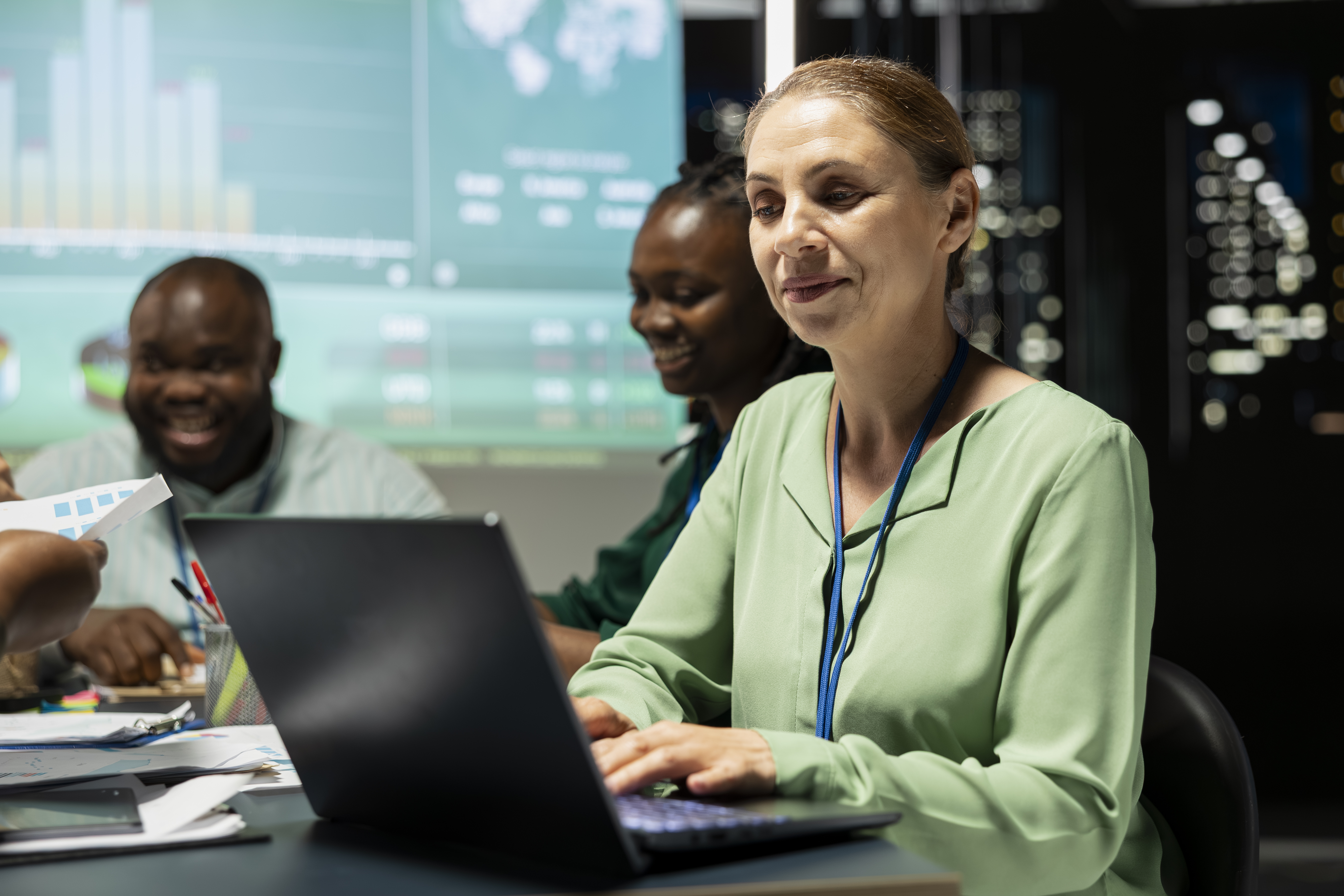 Woman using laptop with financial data dashboards on screens behind.