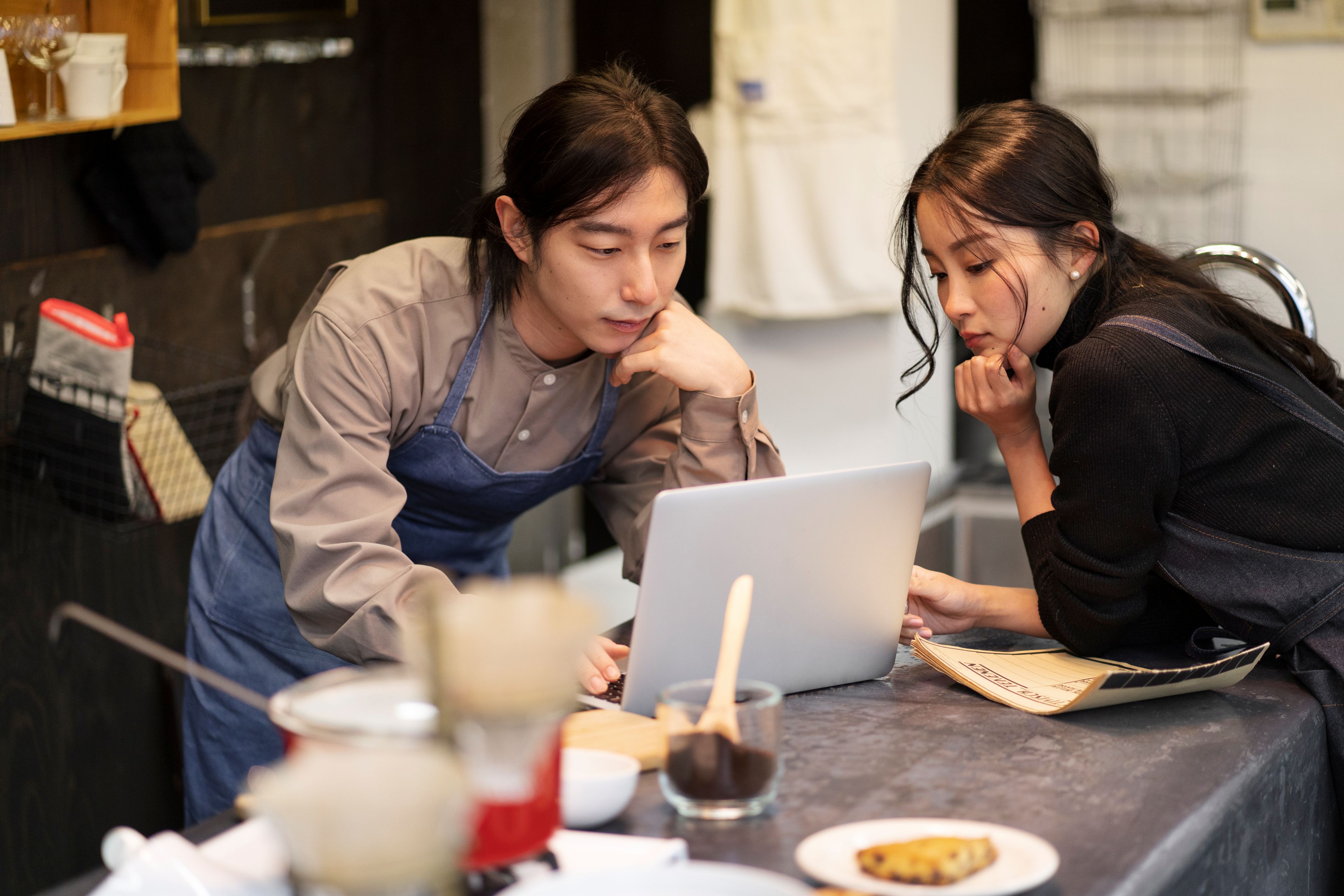 Two people looking at laptop on top of counter with ground coffee and equipment.